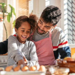 Photo of a smiling african american father and daughter baking in the kitchen and having fun.