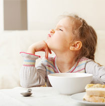 little girl finicky eater not wanting to eat food at table in white bowl - SuperKidsNutrition.com