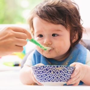baby with blue bib and blue bowl eating veggie dish with sweet potato for babies - SuperKidsNutrition.com