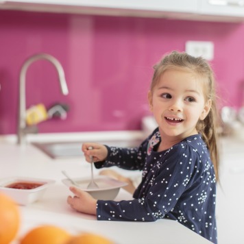 4 year old in kitchen eating food from her sample day of meals for a 4 year old - SuperKids Nutrition