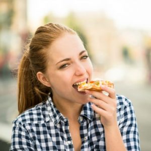 Teenager lifestyle - young woman eating pizza outdoor in street