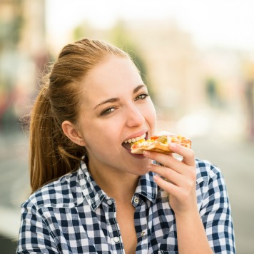 Teenager lifestyle - young woman eating pizza outdoor in street