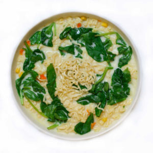 bowl of creamy chicken noodle soup with spinach and noodles on a white background
