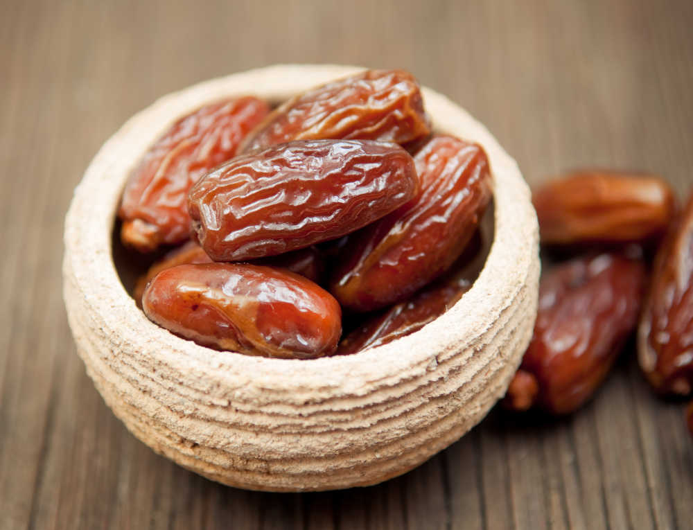 Delicious dates in small bowl on wooden surface for dessert