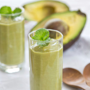 avocado smoothie with mint leaves, sliced half of avocado in the background, with wooden spoons