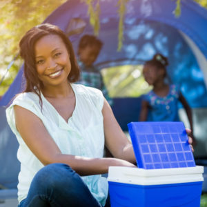 black woman sitting with blue cooler at a camp site