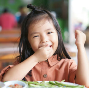 Asian child hungry or kid girl enjoy eating vegetable and delicious food on wood table with happy smiling for morning breakfast or lunch in restaurant or nursery preschool and kindergarten food court