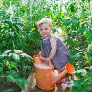 Baby girl waters a plant in greenhouse