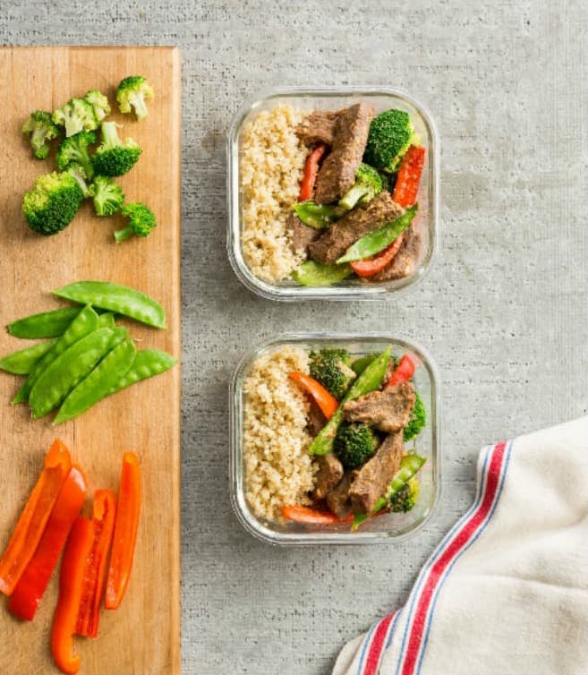 two containers of beef stirfry with colorful veggies on cutting board