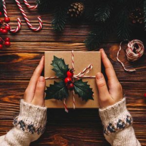 Christmas gifts for parents. Top wiew of woman holding traditional decorated gift box. Wooden table with cane,fir branches, fir cone, and berries