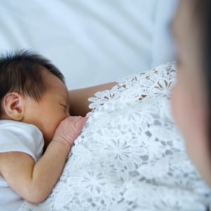 Asian mother holding her newborn daughter while breastfeeding child on the bed