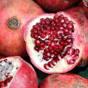 Open pomegrante shows seeds on top of a pile pomegranates